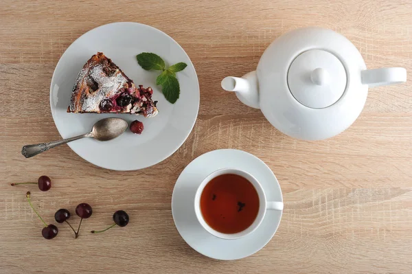 Tabakta klasik çikolatalı kek. Brownie nane yaprağı ile dekore edilmiştir. Sonra bir fincan çay ve bir tabak turta. Taze kirazlar masada. Bir kişiye hizmet ediyor. Yukarıdan görüntüleyin. Close.
