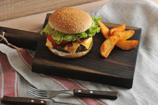 Tahta tahtada sulu çizburger. Cheeseburger doldurma, et pirzama, Çedar peyniri, pastırma, domates, salatalık turşusu, marul ve sos. Sonraki patates dilimleri rustik. Close.