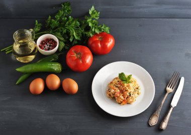 Domates ile geleneksel Türk kızartılmış yumurta pişirme için malzemeler. Çerçeveiçinde, yumurta, domates, acı yeşil biber, yeşillik, zeytinyağı, baharat ve pişmiş çırpılmış yumurta bir tabak. Yukarıdan görüntüle.