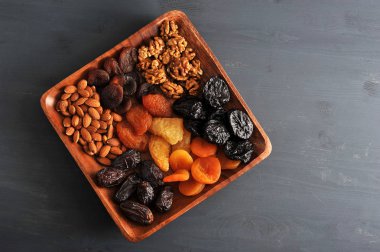 Kurutulmuş meyve ve fındık bir tabakta. Tabakta hurma, kuru erik, kuru kayısı, kuru armut ve şeftali, badem ve ceviz bulunmaktadır. Karanlık bir arka plan. Yukarıdan görüntüleyin. Close. Makro fotoğrafçılık.