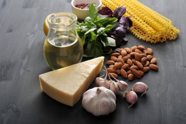 Geleneksel pesto sos hazırlanması için Malzemeler. Çerçeveiçinde, fesleğen, badem, baharat, sarımsak, zeytinyağı, limon, parmesan ve makarna Fusilli lunghi. Koyu ahşap arka plan. Close.