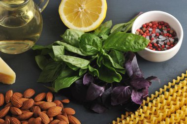 Pesto soslu makarna pişirmek için ihtiyacınız olan her şey. Çerçevede yeşil ve mor fesleğen, badem, parmesan peyniri, limon, baharat, zeytinyağı ve Fusilli lunghi makarna. Karanlık arka plan. Close.