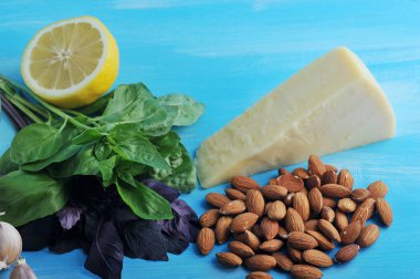 Yeşil pesto sosu için malzemeler. Çerçevede, yeşil fesleğen, badem, yarım limon, parmesan peyniri ve sarımsak karanfil. Mavi ahşap arka plan. Close. Makro fotoğrafçılık.
