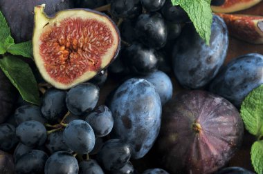 Çerçeve sulu erik, üzüm ve olgun incir ile doldurulur. Meyve ve çilek bir arka plan oluşturur. Kompozisyon nane yaprakları ile desteklenir. Yukarıdan görüntüleyin. Close. Makro fotoğrafçılık.