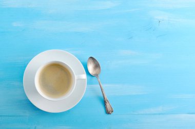 Bir fincan sade kahve ve bir tabak. Bir sonraki çay kaşığı. Mavi ahşap arka plan. Close. Yukarıdan görüntüleyin. Metin için boş alan.