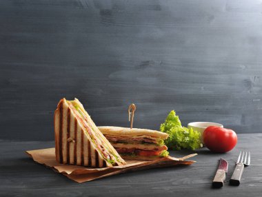 Kraft kağıda bir sandviçin iki yarısı. Sandviç kulübünün dolması jambon, peynir, domates, pastırma, sos ve kızarmış yumurtadan oluşur. Karanlık arka plan. Metnin altına yerleştirin. Close.