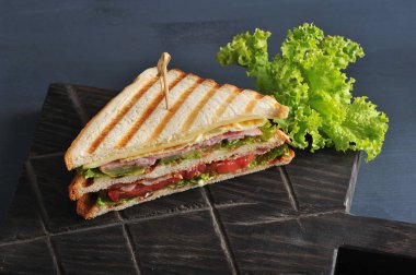 Tahta bir tahta üzerinde üçgen şeklinde bir sandviç yarısı. Sandviç marul yaprağı ile dekore edilmiştir. Koyu ahşap arka plan. Close.