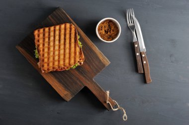 Tahta bir tahta üzerinde beyaz ekmek birkaç dilim Sandviç. Sandviçin dolgusu pastırma, peynir ve jambondan oluşur. Bir sonraki çatal bıçak takımı ve bir fincan hardal. Koyu ahşap arka plan. Yukarıdan görüntüle.