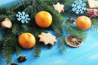 Mavi ahşap arka plan üzerinde Noel kompozisyon. Kürk ağacı dalı mandalina, bisküvi, kurutulmuş portakal dilimleri, anason, tarçın çubukları ve Noel ağacı oyuncakları ile dekore edilmiştir. Close.