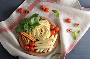 Tahta bir tabakta Chechil peyniri buldum. Çeri domates ve fesleğen yeşilliklerinin yanında. Koyu arka plan ve doku peçetesi. Bir peçete ceviz ve kiraz domates. Close. Yukarıdan görüntüle.