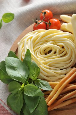 Chechel peynirini pipet ve spagetti şeklinde buldum. Çeri domates ve fesleğen yeşilliklerinin yanında. Arka plan bir peçete ile kaplıdır. Çerçevenin dikey yönü. Close.