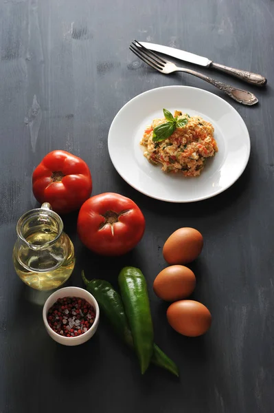 Domates ile geleneksel Türk kızartılmış yumurta pişirme için malzemeler. Çerçevede, tavuk yumurta, domates, acı yeşil biber, zeytinyağı, baharat ve pişmiş çırpılmış yumurta bir tabak. Yukarıdan görüntüle.