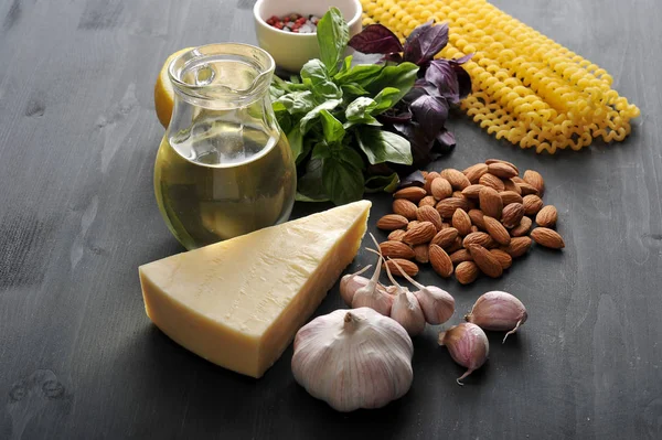 Geleneksel pesto sos hazırlanması için Malzemeler. Çerçeveiçinde, fesleğen, badem, baharat, sarımsak, zeytinyağı, limon, parmesan ve makarna Fusilli lunghi. Koyu ahşap arka plan. Close.