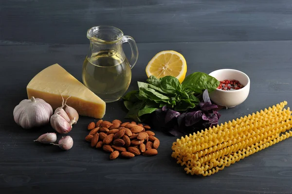 Pesto soslu makarna için malzemeler. Çerçeveiçinde, yeşil ve mor fesleğen, badem, yarım limon, parmesan peyniri, sarımsak, baharat, zeytinyağı ve makarna. Karanlık arka plan. Close.