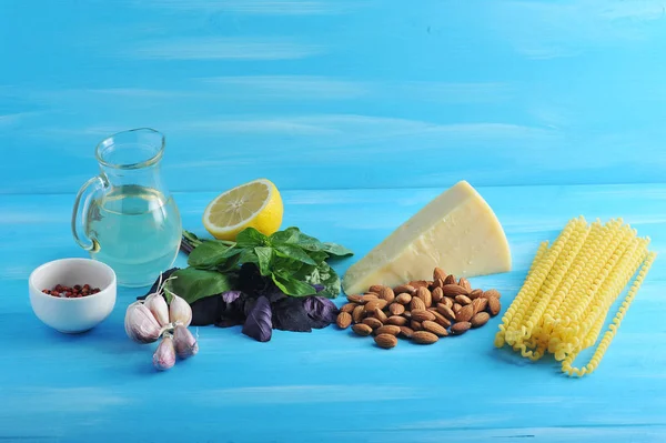 Pesto sos ve makarna için Malzemeler. Çerçeveiçinde, yeşil fesleğen, badem, sarımsak, limon, zeytinyağı, baharat, parmesan peyniri ve makarna Fusilli lunghi bucati bir sürahi. Mavi ahşap arka plan. Close.