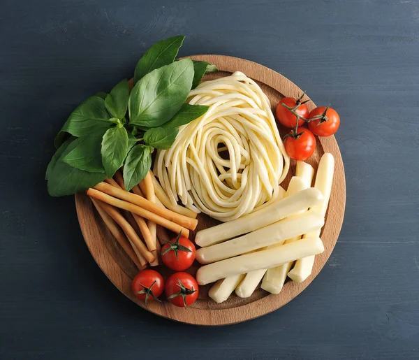 The cheese was crawling on a wooden plate. Cheese in the form of spaghetti, in the form of straws smoked and white. Next to cherry tomatoes and basil greens. Close-up. View from above.