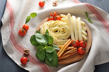 Tahta bir tabakta Chechil peyniri buldum. Çeri domates ve fesleğen yeşilliklerinin yanında. Koyu arka plan ve doku peçetesi. Bir peçete ceviz, fesleğen yaprakları ve kiraz domates. Close. 