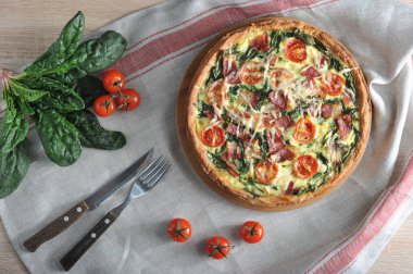 Ispanak, pastırma, kiraz domates ile Klasik Fransız pasta quiche. Çerçeve çatal bıçak, domates, ıspanak. Arka plan bir peçete ile kaplıdır. Close. 
