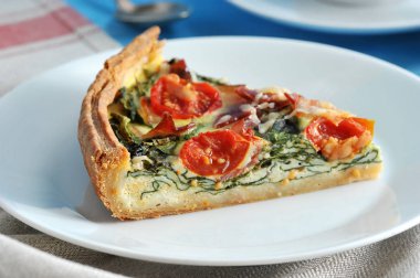 Beyaz tabakta klasik Fransız turta sıcağı. Dolgu bileşimi ıspanak, pastırma, peynir, kiraz domates olduğunu. Arka plan bir peçete ile kaplıdır. Close. Makro fotoğrafçılık.