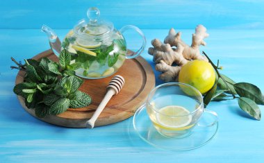 Ahşap bir tepside bir demet yeşil nane ve bir çaydanlık vardır. Bir cam çaydanlık, zencefil, limon ve nane kaynaklanır. Zencefil, limon ve et suyu ile bir fincan kök yakın. Yukarıdan görüntüleyin. Close.