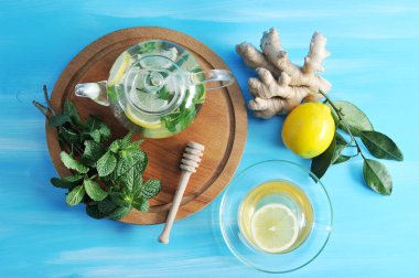 Ahşap bir tepside bir demet yeşil nane ve bir çaydanlık vardır. Bir cam çaydanlık, zencefil, limon ve nane kaynaklanır. Zencefil, limon ve et suyu ile bir fincan kök yakın. Yukarıdan görüntüleyin. Close.