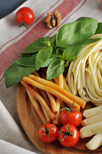 Figured Chechel cheese in the form of straws and spaghetti. Next to cherry tomatoes and basil greens. The background is draped with a napkin. Vertical orientation of the frame. Close-up.