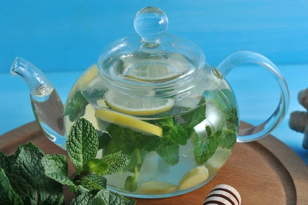 Cam bir çaydanlıkta zencefil içeceği. Nane, zencefil, ballı limondan yapılmış faydalı bir içecek. Mavi ahşap arka plan. Close.