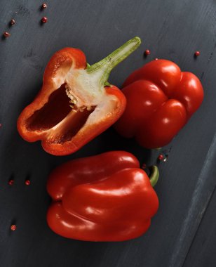 Kırmızı tatlı biber. İki buçuk. Yüzeyde pembe biber bezelye dağınık. Karanlık arka plan. Close. Yukarıdan görüntüleyin. Çerçevenin dikey yönü.