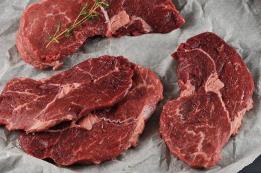 Parşömen kağıdında çiğ biftek. Bifteklerden birinde bir dal kekik var. Yukarıdan görüntüleyin. Close. Makro fotoğrafçılık.