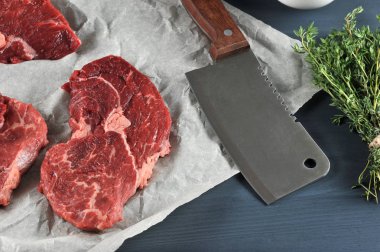 Parşömen kağıdında çiğ biftek. Et kesmek için biftek bıçağının yanında. Çerçevede, bir demet kekik var. Koyu ahşap arka plan. Close. yukarıdan görünüm.