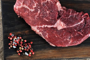 Tahta bir tahtada çiğ biftek. Biftek yanında biber ve büyük tuz vardır. Makro fotoğrafçılık. Yukarıdan görüntüle.