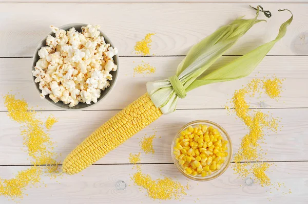 A set of corn. Corn cob, canned corn kernels, popcorn and corn croup. White wooden background. Close-up. View from above.