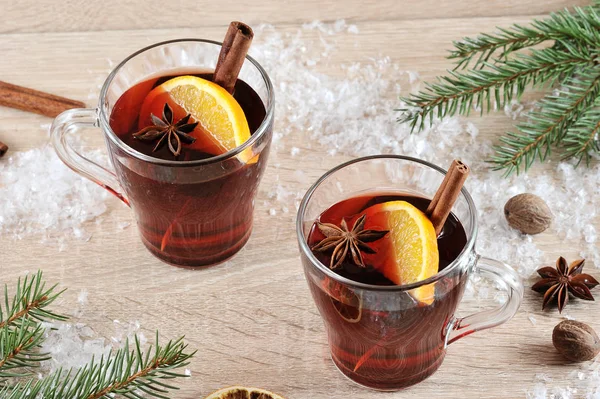 İki bardak, sıcak şarap. İçecek bardak tarçın bir sopa, limon ve anason bir dilim ile dekore edilmiştir. Köknar dalı ve yapay kar çerçevesinde. Açık ahşap arka plan. Close