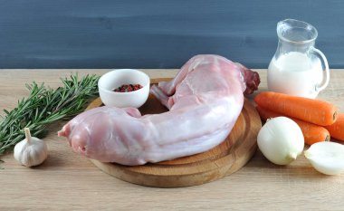 Tahta tahtada ham tavşan. Çerçevede, havuç, soğan, baharat, bir demet biberiye, sarımsak, krema. Biberiye ile tavşan pişirmek için bir set. Açık ahşap arka plan. Close. 