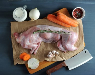 Biberiye ile tavşan pişirme için ayarlanmış çerçevede. Ham bir tavşan kraft kağıda konur. Havuç, soğan, biberiye, sarımsak, baharat, et kesmek için bıçak yanında. Karanlık arka plan. Yukarıdan görüntüle.