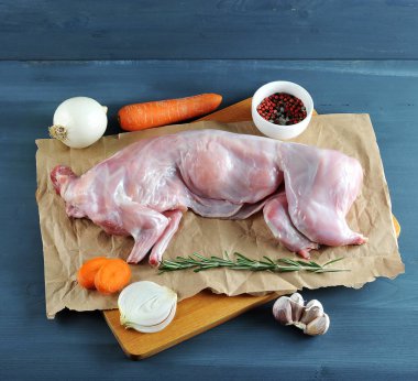 Biberiye ile tavşan pişirmek için bir set. Çerçevede, kraft kağıt üzerinde ham bir tavşan. Havuç, soğan, biberiye, sarımsak, baharat. Koyu ahşap arka plan. 