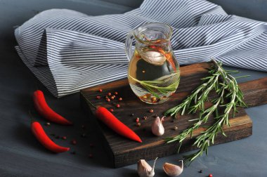 Zeytinyağı ile sürahi. Bir demet biberiye, biber, sarımsak, acı biber. Arka planda bir peçete. Koyu arka plan. 