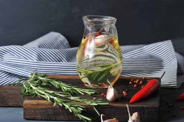 Zeytinyağı ile sürahi. Bir demet biberiye, biber, sarımsak, acı biber. Arka planda bir peçete. Karanlık arka plan. Close.