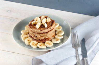 Karabuğday krep bir tabak üzerinde bir slayt ile kaplıdır. Krep çikolata şurubu ile bir muz ile dekore edilmiştir. Muz parçalarıyla kaplı bir tabakta kreplerin etrafında. Ahşap arka plan. Close.