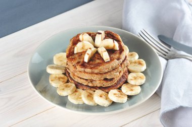 Karabuğday krep bir tabak üzerinde bir slayt ile kaplıdır. Krep çikolata şurubu ile bir muz ile dekore edilmiştir. Muz parçalarıyla kaplı bir tabakta kreplerin etrafında. Ahşap arka plan. Close.