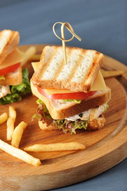 Ahşap bir tepside kızarmış beyaz ekmek ve patates kızartmasından yapılmış mini sandviçler vardır. Sandviçin dolgusu ızgara tavuk, salata, peynir, domates diliminden oluşur. Karanlık arka plan. Closeup.