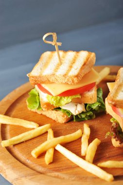 Ahşap bir tepside kızarmış beyaz ekmek ve patates kızartmasından yapılmış mini sandviçler vardır. Sandviçin dolgusu ızgara tavuk, salata, peynir, domates diliminden oluşur. Karanlık arka plan. Closeup.