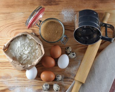 Pişirme için ayarlayın. Çerçevede, süt, un, şeker, bıldırcın yumurtası ve tavuk yumurtası, oklava, bir un elemek bir sürahi. Ahşap arka plan un serpilir. Close. Yukarıdan görüntüle.