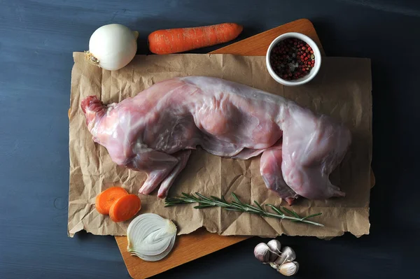 Biberiye ile tavşan pişirmek için bir set. Çerçevede, kraft kağıt üzerinde ham bir tavşan. Havuç, soğan, biberiye, sarımsak, baharat. Koyu ahşap arka plan. Yukarıdan görüntüle.