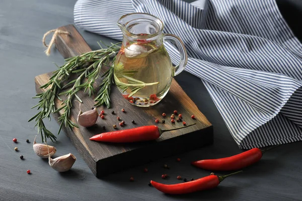 Zeytinyağı ile sürahi. Yağ, biber, biberiye, sarımsak ekledi. Kompozisyon biberiye, bezelye biber, sarımsak, acı biber bir demet ile tamamlanmaktadır. Arka planda bir peçete. 