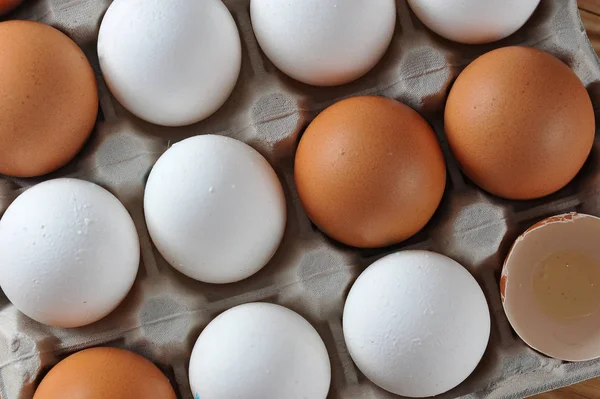 Chicken eggs are raw in the tray. The shell is white and brown in eggs. In one section is an egg shell. View from above. Close-up. Macro photography.