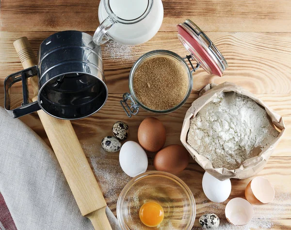 Pişirme için ayarlayın. Resimde, süt, un, bıldırcın yumurtası ve yumurta, bir oklava, bir un elemek, bir kase protein ile bir sarısı ve bir yumurta kabuğu bir sürahi. Ahşap arka plan. Close. Yukarıdan görüntüle.