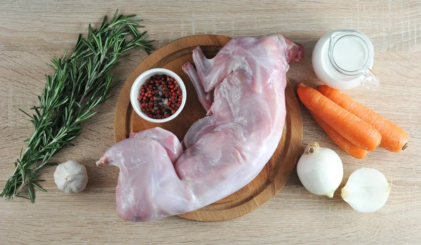 Raw rabbit on a wooden board. In the frame, carrots, onion, spices, a bunch of rosemary, garlic, cream. Light wooden background. View from above. Close-up. — Stock Image Raw Rabbit Wooden Board Frame Carrots Onion Spices Bunch Rosemary Stock Picture