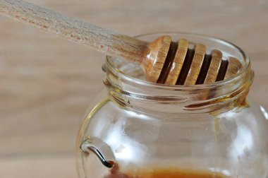 Ballı cam kavanoz. Bankanın kenarında özel bir bal çubuğu vardır. Açık arka plan. Close. Makro fotoğrafçılık.