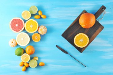 Narenciye bileşimi. Çerçevede portakal, mandalina, limon, limon, kumquat, pembe ve sarı greyfurt. Tahta tahtanın yanında bir portakal ve yarım portakal var. Mavi ahşap arka plan. Yukarıdan görüntüle